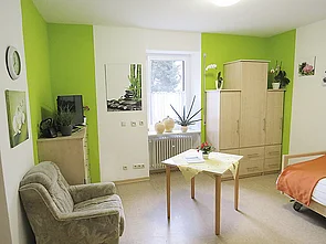 Helles Zimmer im Haus Wichern mit Fenster, Bett, Schrank, Tisch und einem Sofa