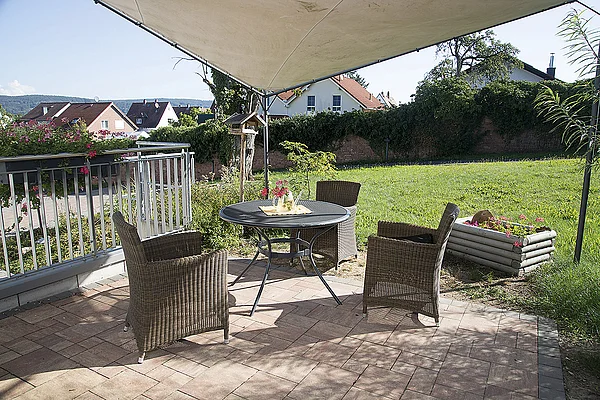 Terrasse des 'Haus im Park' mit Sonnenschutz, Tisch und Stühlen, im Hintergrund eine große Wiese und eine mit Efeu bewachsene Mauer