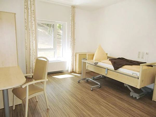 Helles Bewohnerzimmer mit Fenster, Pflegebett, Tisch und Schrank